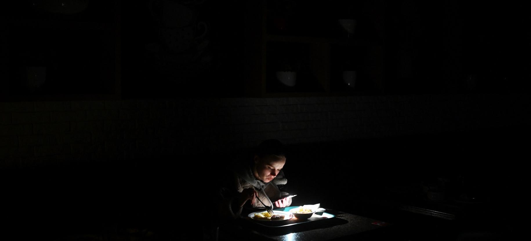 Una ragazza utilizza la torcia del suo smartphone per vedere il cibo nel piatto durante un blackout a Kiev, Ucraina.   Nutrire il mondo. La sfida globale dell'alimentazione